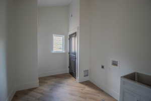 Clothes washing area with hookup for an electric dryer, hookup for a washing machine, light wood-style flooring, and baseboards