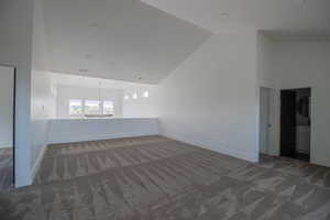 Spare room with a chandelier, carpet, vaulted ceiling, and baseboards