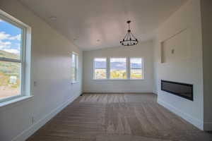 Unfurnished living room with a chandelier, plenty of natural light, light carpet, baseboards, and vaulted ceiling