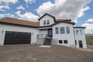 View of front of property featuring an attached garage, asphalt driveway, roof with shingles, and board and batten siding