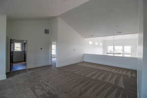 Carpeted empty room with a chandelier, baseboards, and high vaulted ceiling