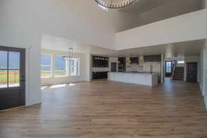 Unfurnished living room featuring a towering ceiling, light wood-type flooring, a sink, baseboards, and stairs