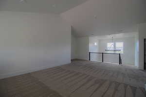 Unfurnished room with light colored carpet, a chandelier, baseboards, and vaulted ceiling