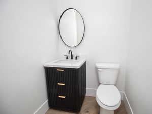 Half bath featuring wood finished floors, toilet, vanity, and baseboards