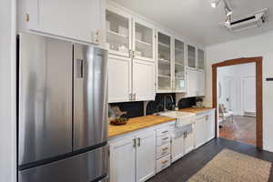 Kitchen featuring freestanding refrigerator, a sink, butcher block counters, white cabinetry, and glass insert cabinets