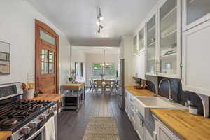 Kitchen featuring appliances with stainless steel finishes, butcher block countertops, a sink, white cabinetry, and ornamental molding