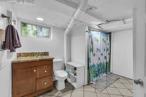 Bathroom with a textured ceiling, tile patterned flooring, toilet, a shower with curtain, and vanity