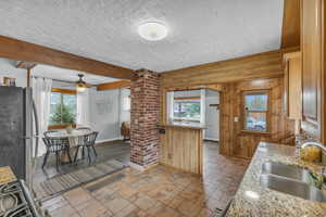 Kitchen with freestanding refrigerator, a sink, ornate columns, healthy amount of natural light, and wooden walls
