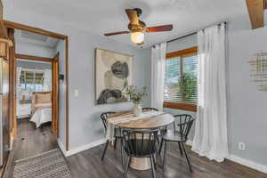 Dining room with healthy amount of natural light, dark wood-style flooring, ceiling fan, baseboards, and a textured ceiling