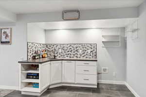 Kitchen with a sink, open shelves, dark countertops, decorative backsplash, and white cabinetry
