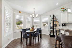 Dining area featuring a chandelier, healthy amount of natural light, dark wood-style floors, baseboards, and vaulted ceiling
