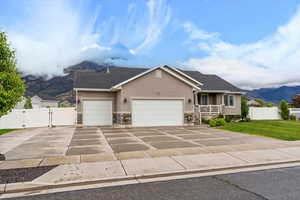 View of front of home with stucco siding, a gate, stone siding, a garage, and driveway
