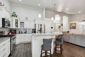 Kitchen featuring stainless steel appliances, a kitchen breakfast bar, dark wood-style flooring, open floor plan, and a towering ceiling