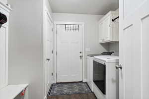 Clothes washing area featuring washing machine and dryer, cabinet space, wood finished floors, and baseboards