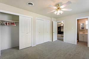 Unfurnished bedroom featuring light colored carpet, multiple closets, a textured ceiling, baseboards, and a sink