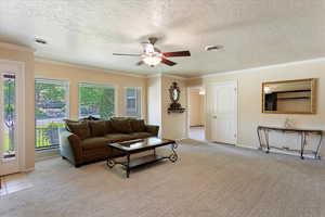 Living room featuring light carpet, a ceiling fan, ornamental molding, a textured ceiling, and baseboards