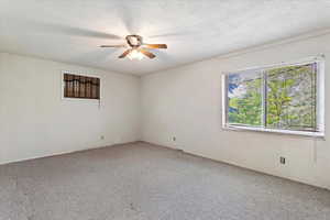 Unfurnished room with ceiling fan, light colored carpet, and a textured ceiling