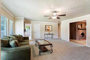 Carpeted living area with a ceiling fan, a fireplace, a textured ceiling, ornamental molding, and baseboards