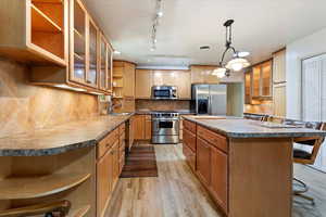 Kitchen with open shelves, appliances with stainless steel finishes, light wood finished floors, a center island, and a sink