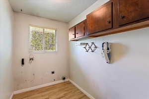 Laundry area featuring cabinet space, electric dryer hookup, light wood-style floors, hookup for a washing machine, and baseboards