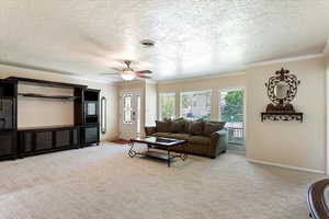 Carpeted living area with a textured ceiling, ceiling fan, baseboards, and ornamental molding