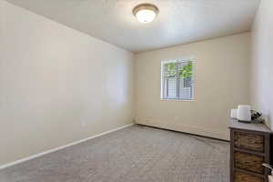 Carpeted empty room with a baseboard radiator, a textured ceiling, and baseboards