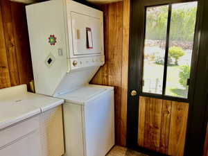 Clothes washing area with stacked washer / dryer, healthy amount of natural light, and wood walls