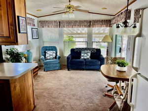 Carpeted living room with a textured ceiling, ornamental molding, ceiling fan, and lofted ceiling