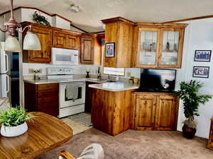 Kitchen with white appliances, a sink, ornamental molding, brown cabinets, and light carpet