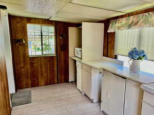 Kitchen featuring white microwave, wood walls, light countertops, and white cabinetry