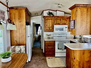 Kitchen featuring white appliances, crown molding, a sink, brown cabinetry, and carpet floors