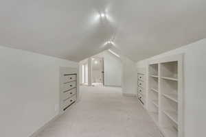 Bonus room with lofted ceiling, light colored carpet, and baseboards