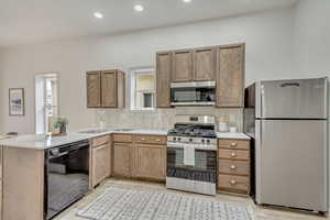Kitchen with appliances with stainless steel finishes, a sink, backsplash, light wood-style flooring, and light countertops