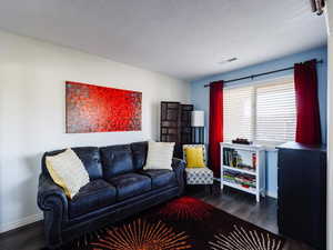 Living room with dark wood-style floors, baseboards, and a textured ceiling