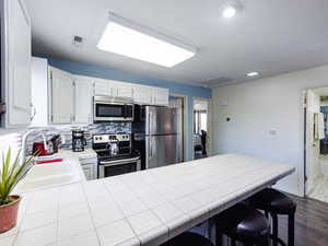 Kitchen with appliances with stainless steel finishes, a sink, backsplash, a peninsula, and tile counters