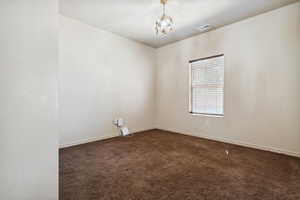 Unfurnished room featuring dark colored carpet, a chandelier, and baseboards