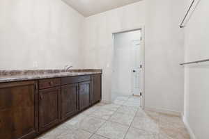 Kitchen featuring dark brown cabinetry, a sink, baseboards, and light tile patterned flooring