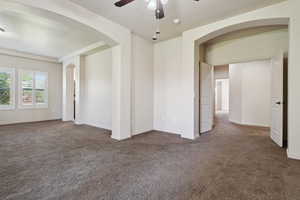 Empty room with dark carpet, a ceiling fan, arched walkways, and baseboards