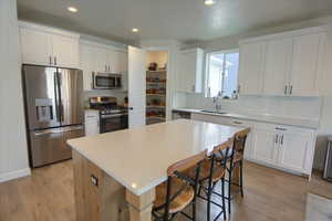 Kitchen with stainless steel appliances, a sink, decorative backsplash, white cabinets, and recessed lighting