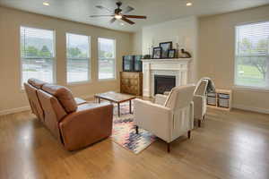 Living room featuring baseboards, light wood-style flooring, ceiling fan, a glass covered fireplace, and recessed lighting