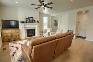 Living room featuring a ceiling fan, light wood finished floors, a glass covered fireplace, baseboards, and recessed lighting