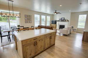 Kitchen featuring light wood finished floors, a chandelier, a glass covered fireplace, a ceiling fan, and hanging light fixtures