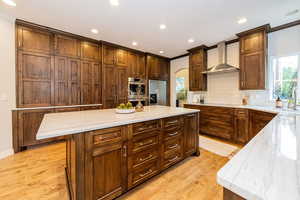 Kitchen featuring wall chimney range hood, appliances with stainless steel finishes, a sink, arched walkways, and ornamental molding