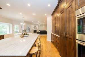 Kitchen with crown molding, recessed lighting, light wood-type flooring, a kitchen breakfast bar, and light stone counters