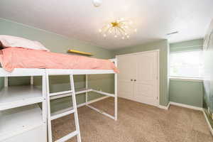 Unfurnished bedroom featuring carpet floors, baseboards, a chandelier, a textured ceiling, and a closet