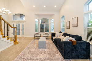 Carpeted living room with a high ceiling, a chandelier, stairway, baseboards, and recessed lighting