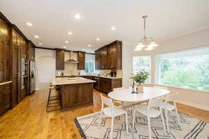 Kitchen with stainless steel appliances, crown molding, wall chimney exhaust hood, a center island, and recessed lighting