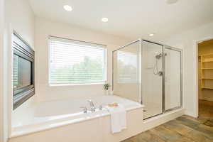 Bathroom featuring a shower stall, a bath, a spacious closet, recessed lighting, and stone finish floors