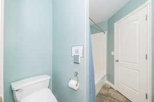 Bathroom with toilet, stone finish floors, tub / shower combination, and baseboards