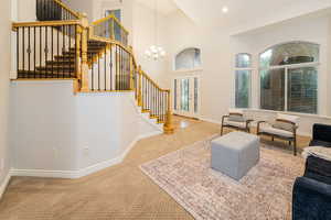 Carpeted living room featuring stairs, baseboards, a chandelier, high vaulted ceiling, and french doors